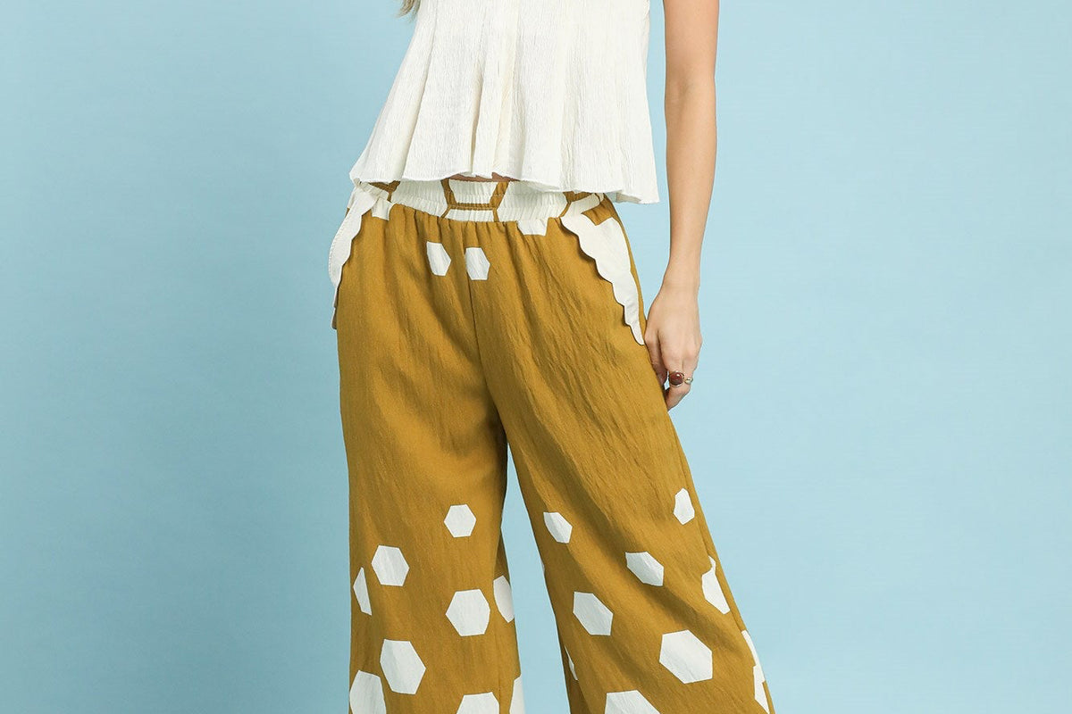 Woman wearing a white top and golden yellow patterned pants against a light blue background